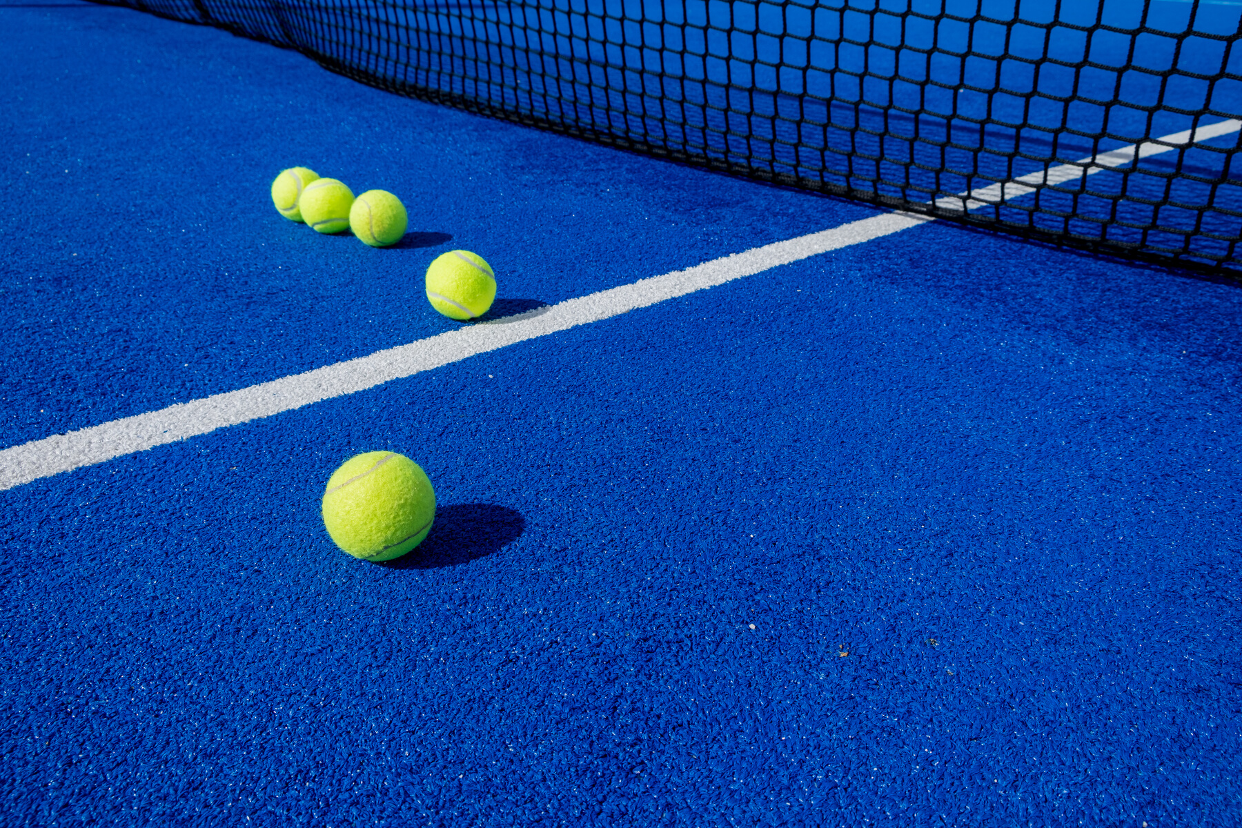 five paddle tennis balls and the net of a blue paddle tennis court, selective focus
