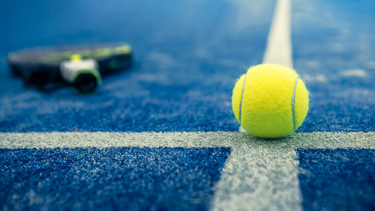 Yellow Ball on Floor behind Paddle Net in Blue Court Outdoors. Padel Tennis